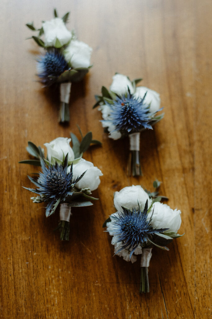 Boutonnière blanche et bleue, mélange de chardon et roses branchues blanches