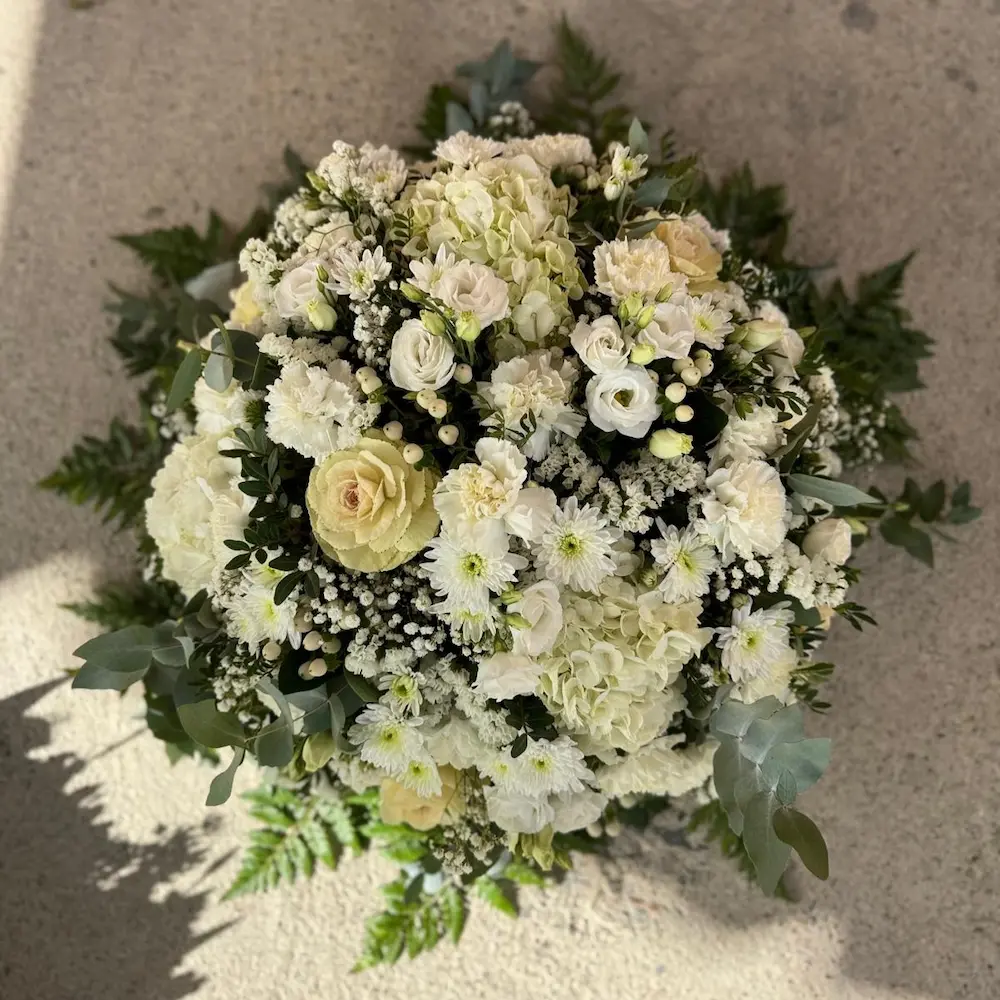 Coussin rond de fleurs dans les tons blanc et vert, mélange d'hortensia, choux, rose, oeillet, lisianthus, statice, eucalyptus, chrysanthème